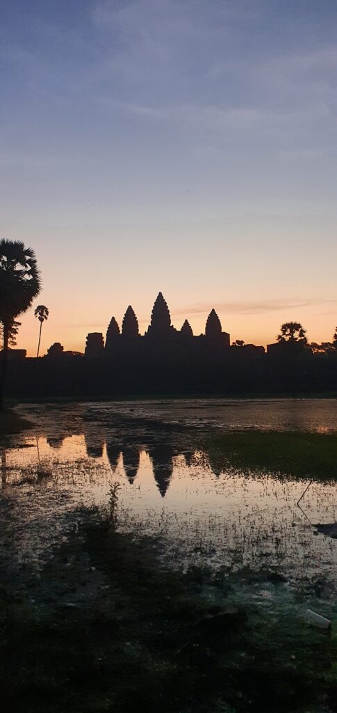 Silhouette of Angkor Wat at sunrise with the temple reflected in a calm pool.